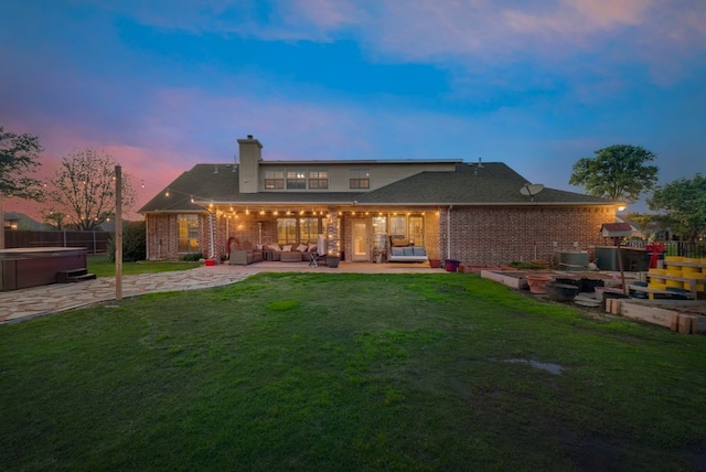 back of house at dusk with a hot tub, a patio area, brick siding, a yard, and an outdoor living space