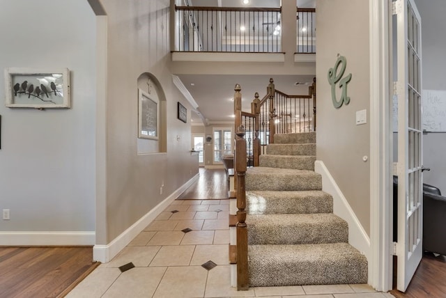 foyer with baseboards, crown molding, a towering ceiling, arched walkways, and stairway