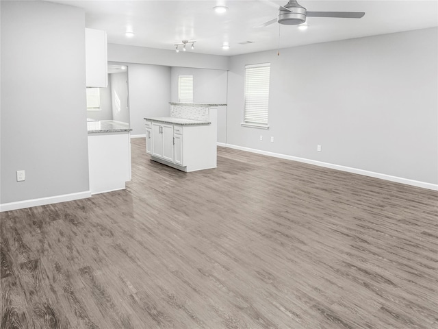 unfurnished living room with ceiling fan, light wood-style flooring, and baseboards
