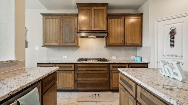 kitchen with under cabinet range hood, light stone countertops, decorative backsplash, and gas cooktop