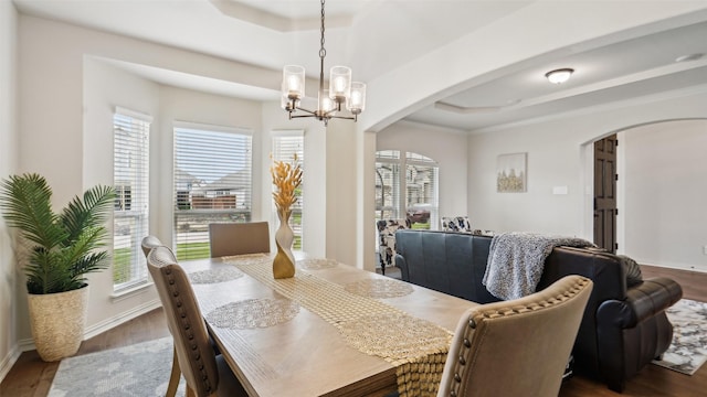 dining area featuring wood finished floors, a raised ceiling, and arched walkways