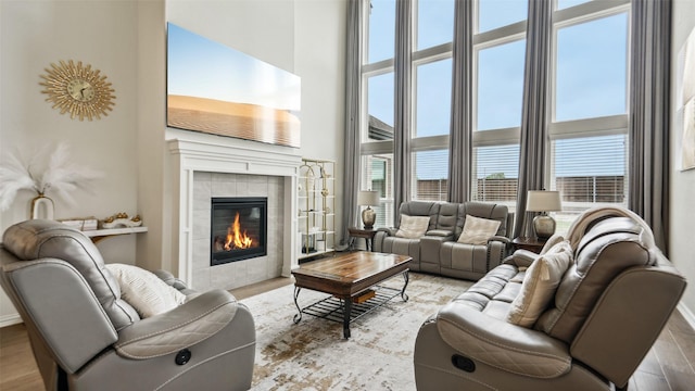 living room with baseboards, a tiled fireplace, wood finished floors, and a towering ceiling