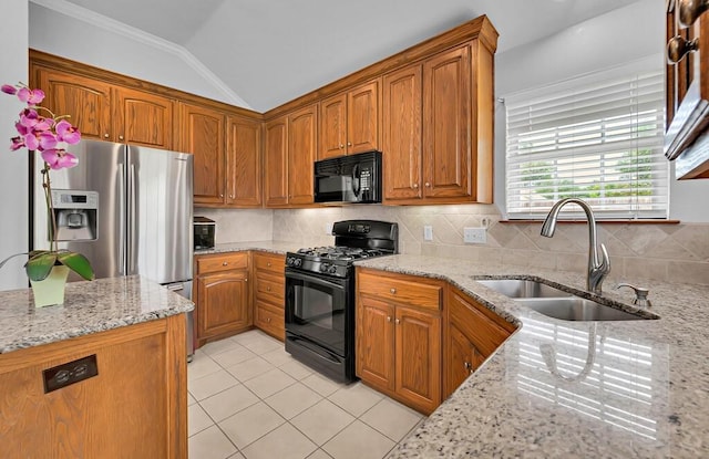 kitchen with a sink, lofted ceiling, tasteful backsplash, light stone counters, and black appliances