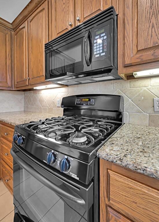 kitchen with light stone counters, brown cabinetry, decorative backsplash, and black appliances