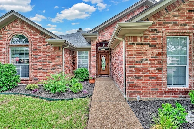 property entrance featuring roof with shingles and brick siding