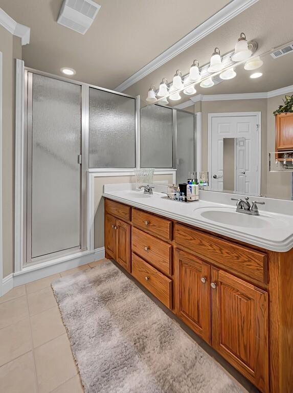 bathroom featuring a sink, visible vents, crown molding, a shower stall, and double vanity
