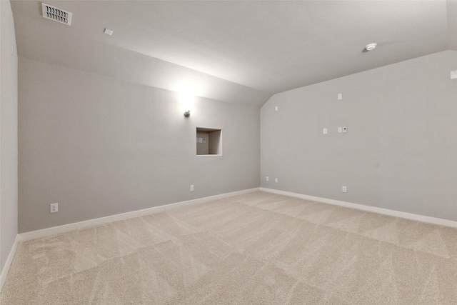 empty room with lofted ceiling, baseboards, visible vents, and light colored carpet