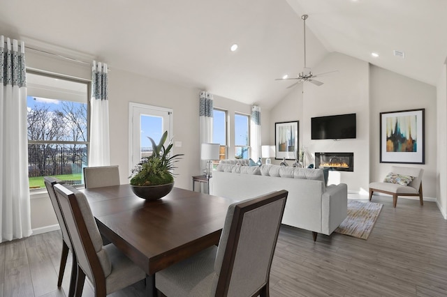 dining space with wood finished floors, high vaulted ceiling, ceiling fan, baseboards, and a glass covered fireplace