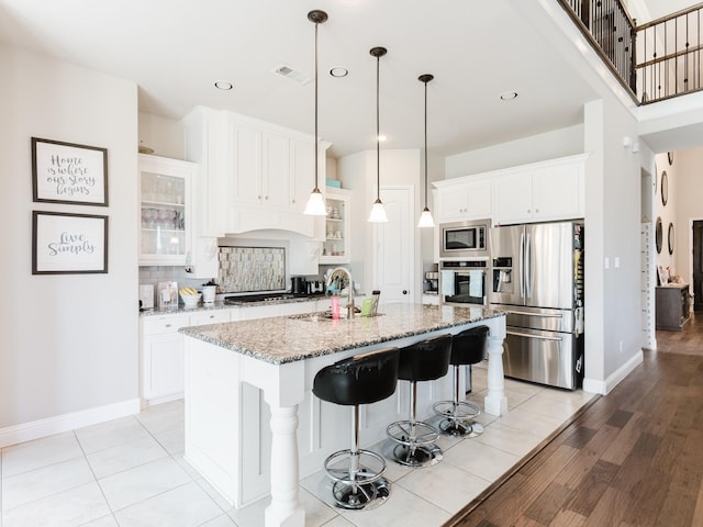 5932 Folsum Pl, Mckinney, TX 75070 - kitchen featuring glass insert cabinets, a kitchen island with sink, visible vents, appliances with stainless steel finishes, and decorative backsplash