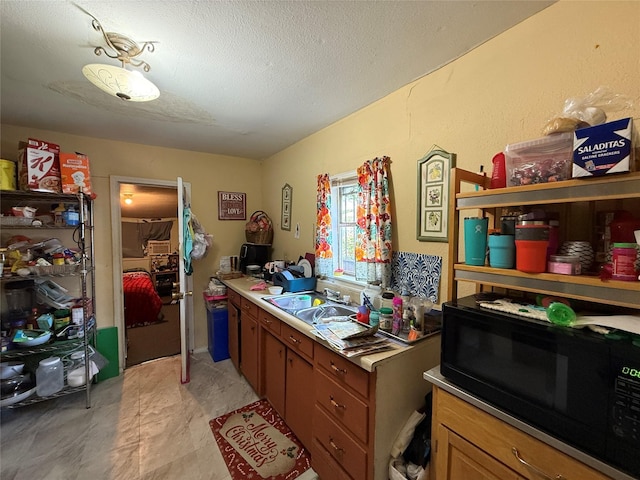 kitchen with a sink, a textured ceiling, black microwave, and brown cabinets