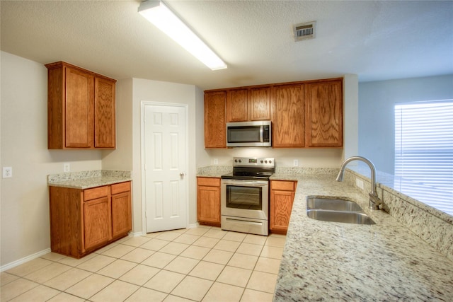 kitchen with light tile patterned floors, visible vents, a sink, brown cabinets, and stainless steel appliances