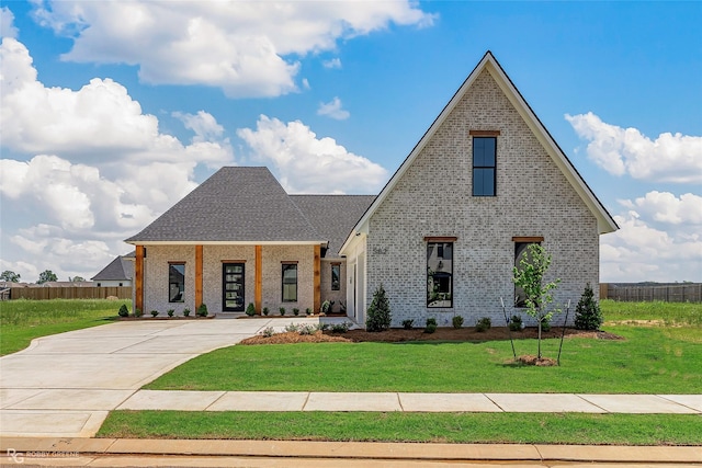 view of front facade with brick siding, roof with shingles, fence, and a front yard