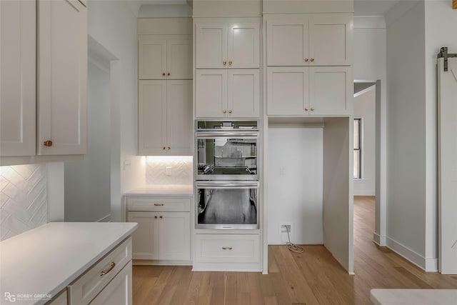 kitchen with tasteful backsplash, stainless steel double oven, light wood-type flooring, light countertops, and white cabinets