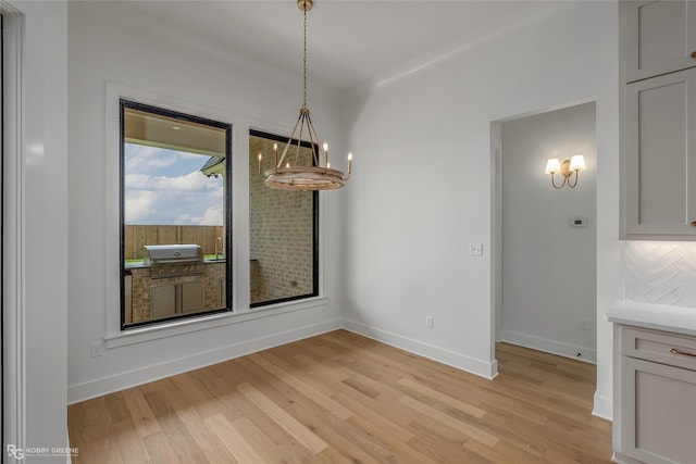 unfurnished dining area with a chandelier, baseboards, and light wood-style floors
