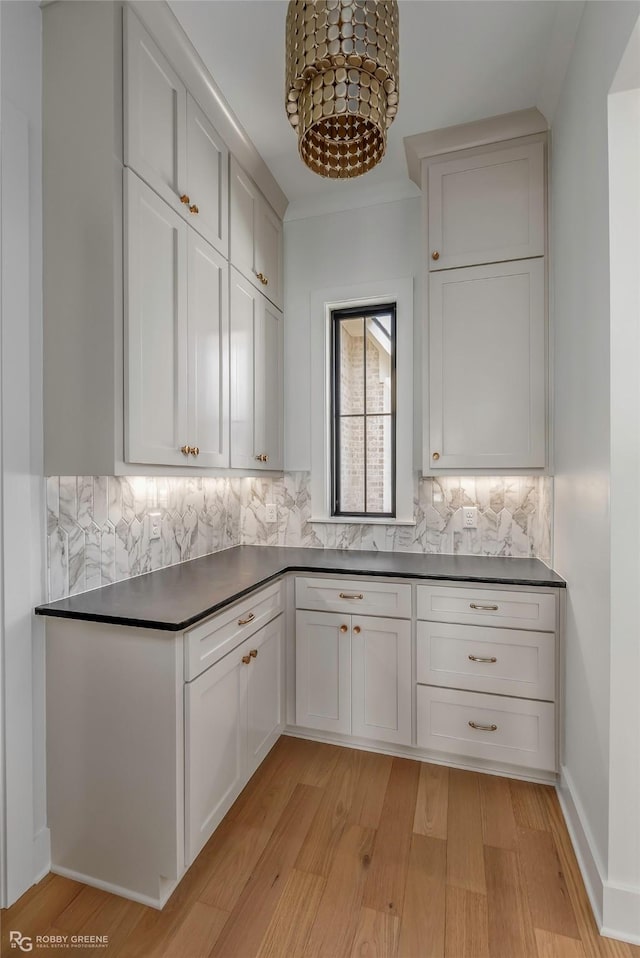 kitchen with dark countertops, light wood-type flooring, decorative backsplash, and white cabinetry