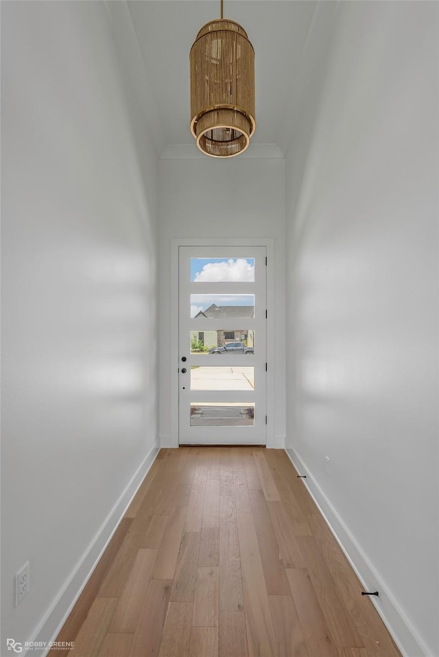 doorway to outside with wood finished floors, baseboards, and ornamental molding
