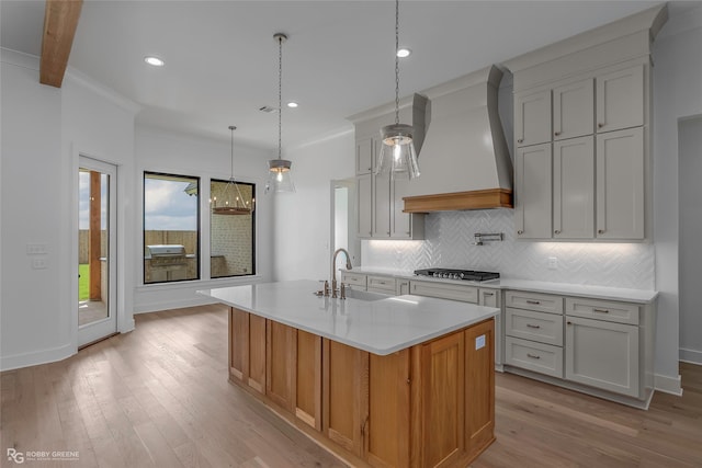 kitchen featuring a sink, custom exhaust hood, light wood-style flooring, backsplash, and light countertops