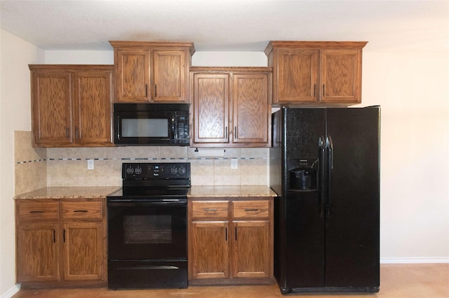 kitchen with brown cabinets, tasteful backsplash, light stone countertops, and black appliances