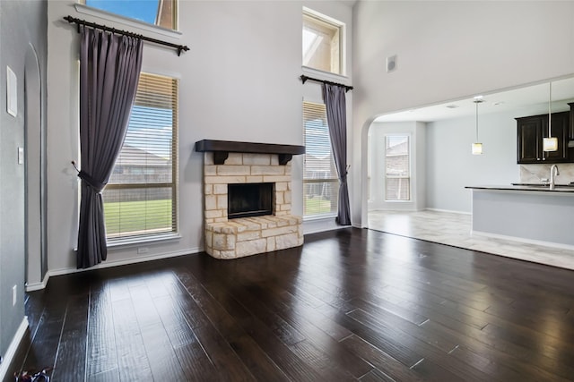 1112 Crest Ridge Dr, Glenn Heights, TX 75154 - unfurnished living room featuring a high ceiling, a stone fireplace, baseboards, wood finished floors, and arched walkways