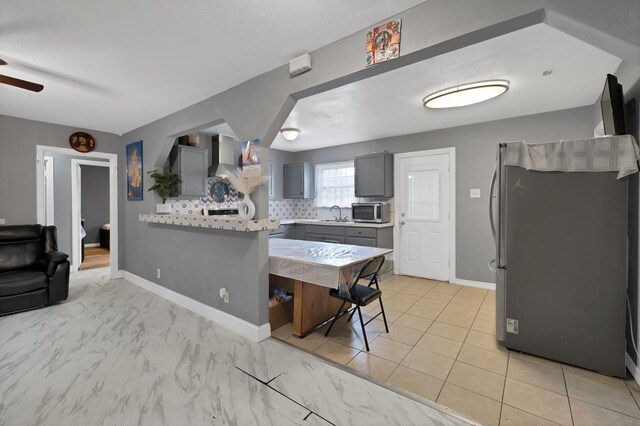 7810 Maxwell Ave, Dallas, TX 75217 - kitchen with gray cabinetry, a peninsula, wall chimney exhaust hood, backsplash, and stainless steel appliances