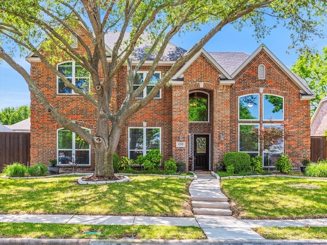 traditional-style house featuring fence, a front lawn, and brick siding