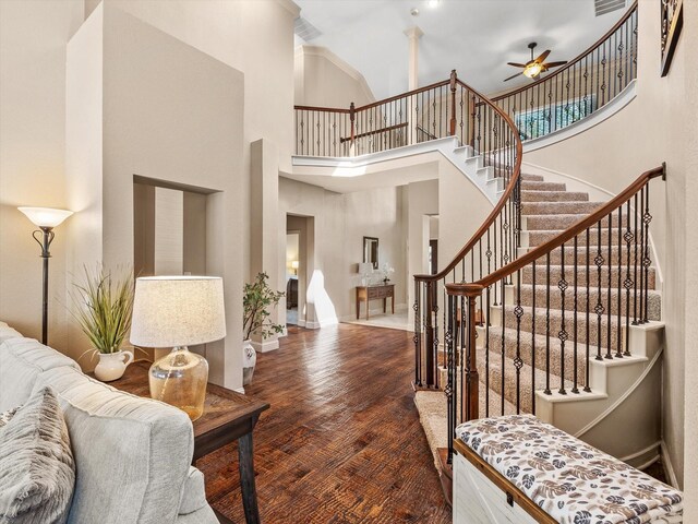 foyer entrance with visible vents, ceiling fan, stairs, wood finished floors, and a high ceiling