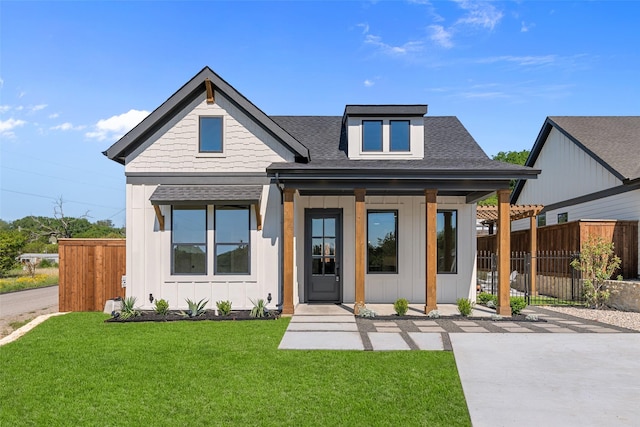 view of front facade with board and batten siding, roof with shingles, a front lawn, and fence