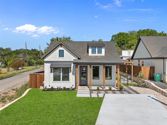modern farmhouse with covered porch, fence, a front lawn, board and batten siding, and roof with shingles