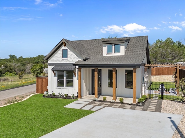 view of front facade with board and batten siding, fence, a front yard, a porch, and roof with shingles