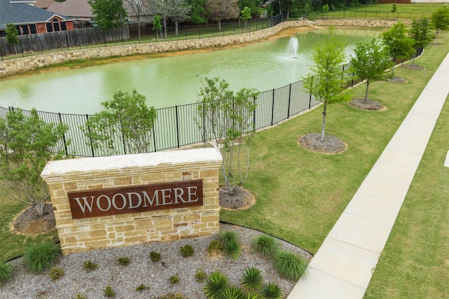 community sign with a water view, a yard, and fence