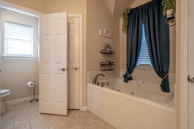 bathroom with toilet, lofted ceiling, a tub with jets, tile patterned flooring, and baseboards