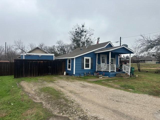 rear view of house featuring covered porch, dirt driveway, fence, and a lawn