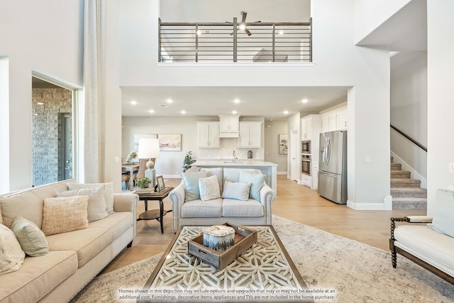 living room featuring recessed lighting, stairway, light wood finished floors, a high ceiling, and baseboards