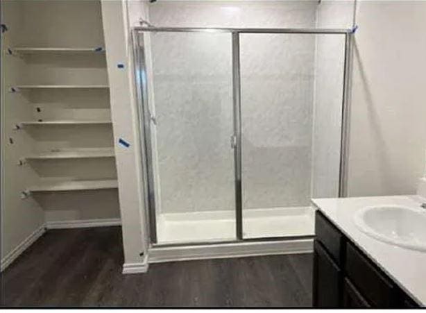 full bath with wood finished floors, vanity, a spacious closet, a shower stall, and baseboards