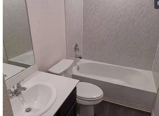 bathroom featuring toilet, wood finished floors, shower / tub combination, a textured wall, and vanity
