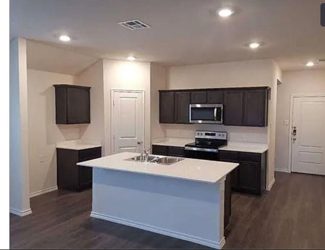 kitchen featuring dark wood finished floors, visible vents, a sink, a center island with sink, and stainless steel appliances
