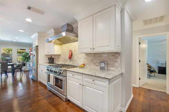 kitchen featuring stainless steel appliances, wall chimney exhaust hood, ornamental molding, white cabinetry, and dark wood-type flooring