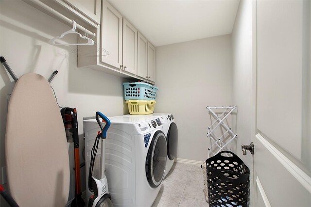 laundry area featuring separate washer and dryer, cabinet space, light tile patterned floors, and baseboards