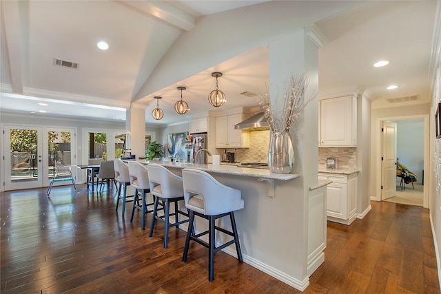 kitchen with backsplash, wall chimney range hood, a breakfast bar, white cabinetry, and recessed lighting