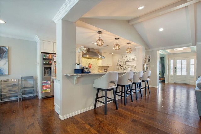 kitchen with stainless steel fridge, wall chimney exhaust hood, recessed lighting, a breakfast bar area, and white cabinetry