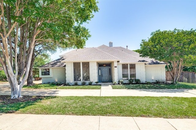 single story home with roof with shingles, fence, brick siding, a front yard, and a chimney