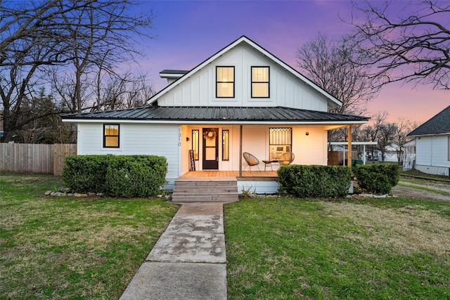 view of front facade featuring board and batten siding, covered porch, fence, and a front yard