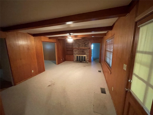 unfurnished living room with wood walls, a ceiling fan, and beamed ceiling