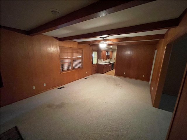 spare room with wood walls, light colored carpet, visible vents, ceiling fan, and beamed ceiling