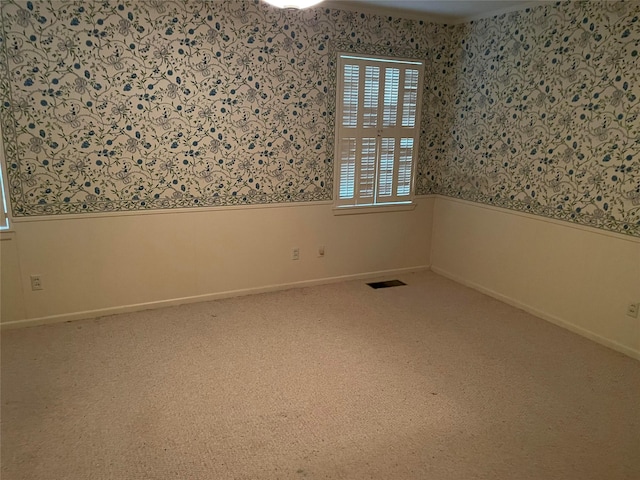 spare room featuring wallpapered walls, carpet floors, visible vents, baseboards, and wainscoting
