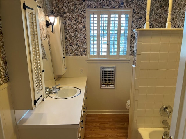 bathroom featuring toilet, wood finished floors, wallpapered walls, vanity, and shower / bathing tub combination