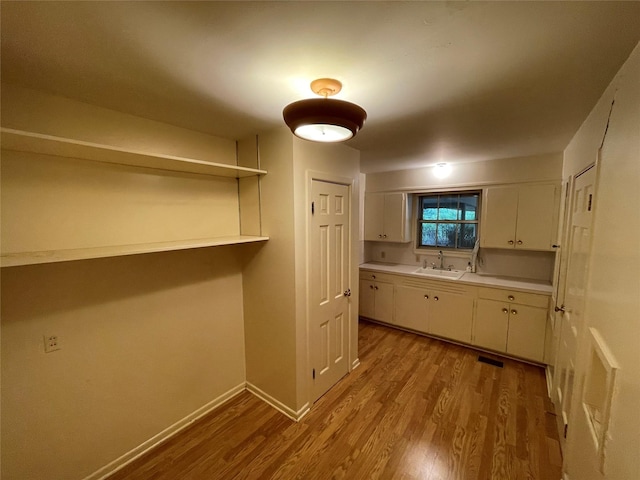 kitchen featuring visible vents, a sink, wood finished floors, light countertops, and white cabinets