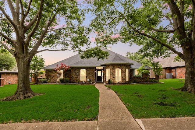 view of front facade featuring roof with shingles, a chimney, brick siding, and a front yard