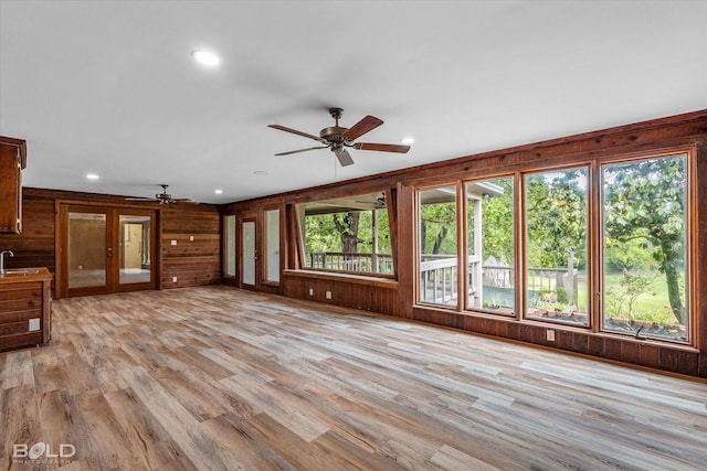 unfurnished living room featuring light wood finished floors, a ceiling fan, a sink, wood walls, and recessed lighting