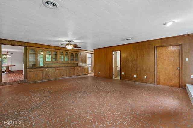 unfurnished living room with wooden walls, visible vents, and ceiling fan